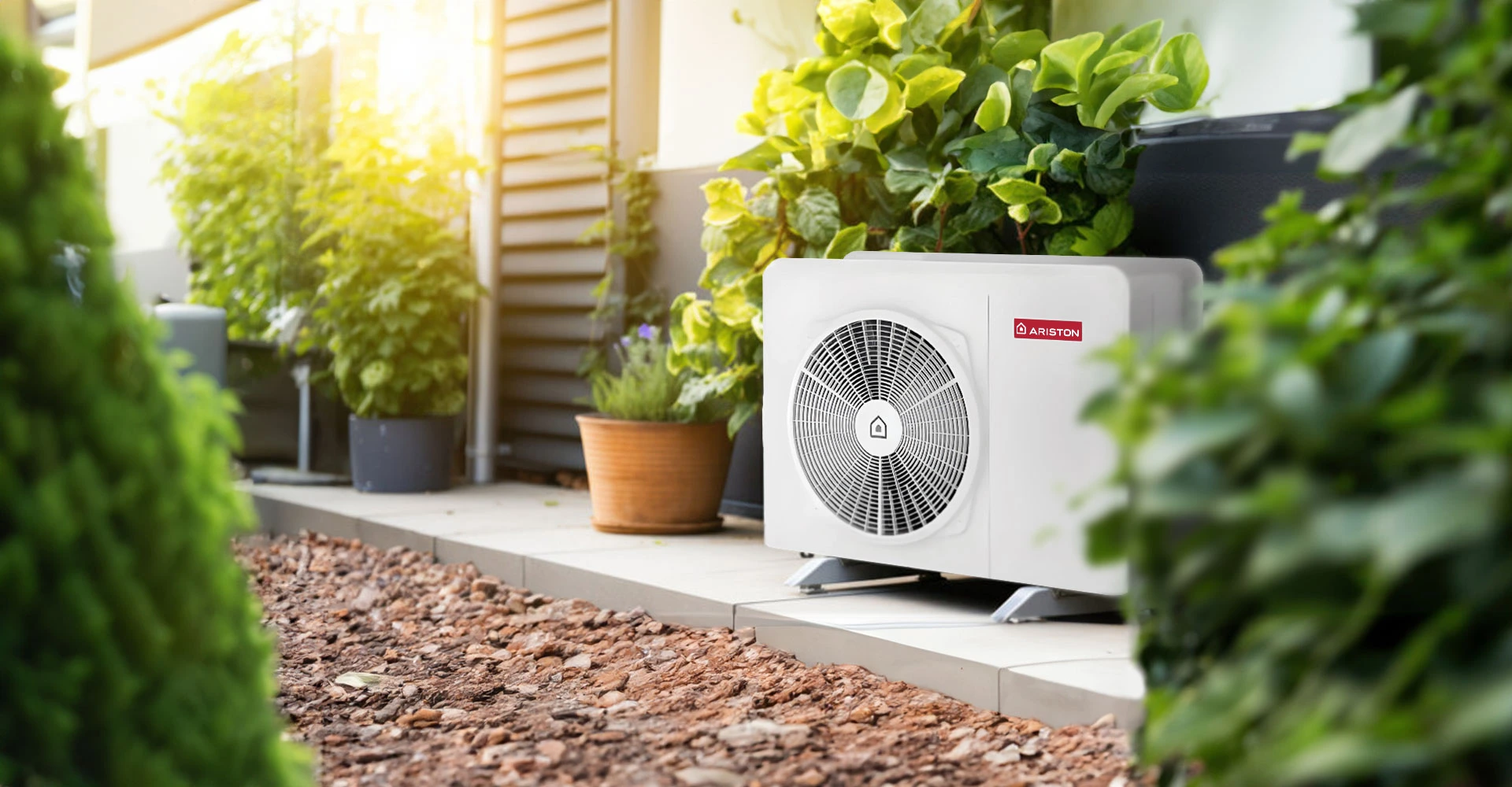 An Ariston outdoor heat pump beside a home and garden plants