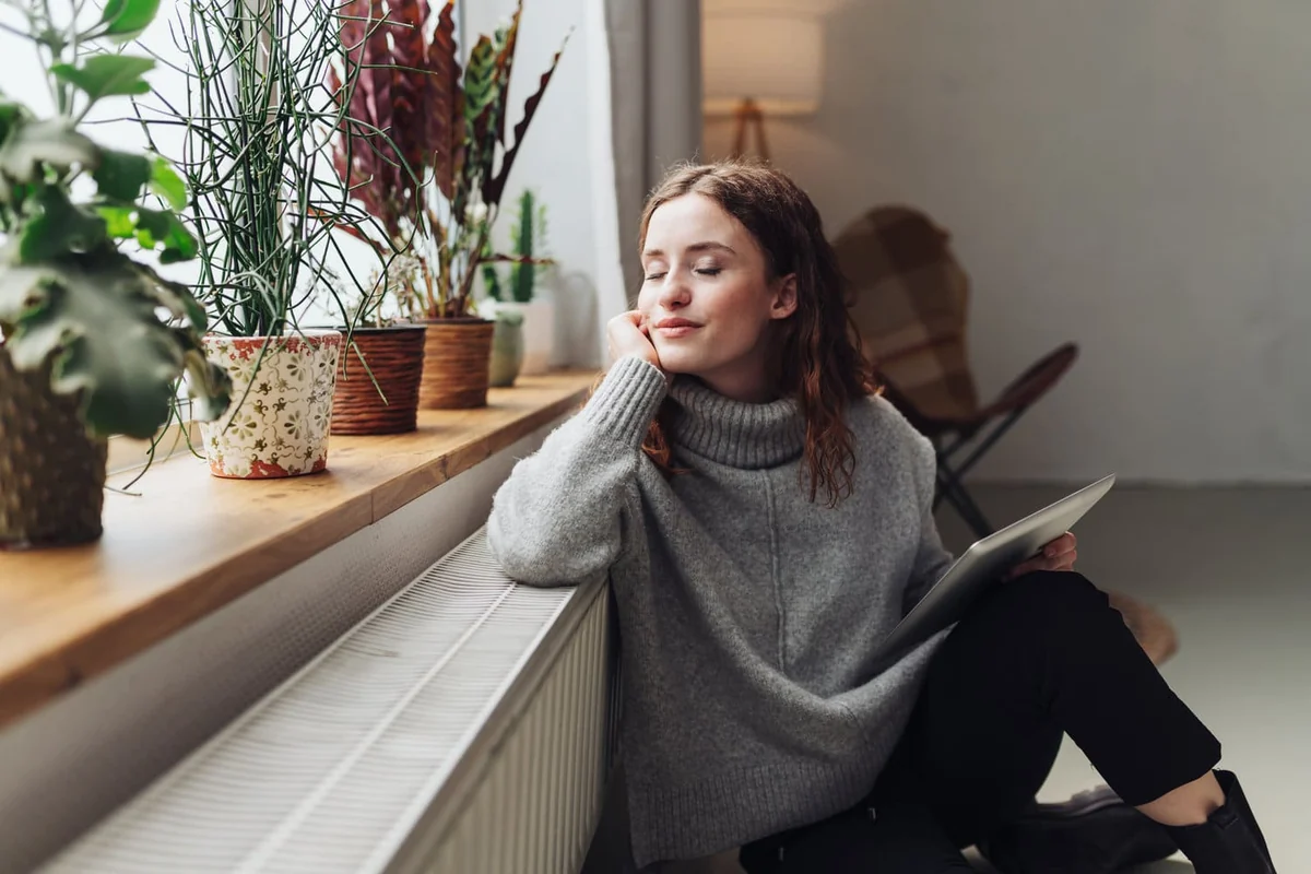 A woman relaxing in a warm home beside a radiator and houseplants